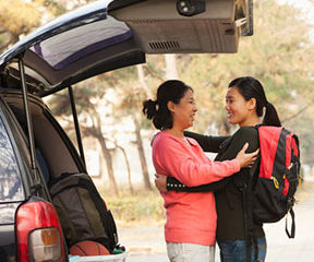 Mother and daughter hugging goodbye by a car.