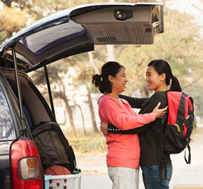 Mother and daughter hugging goodbye by a car.